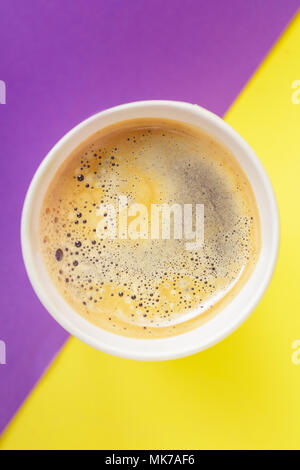 Vue du dessus de l'emporter, boisson chaude dans la tasse thermo ouvert sur fond jaune et violet vibrant. Cafe crema de la mousse sur le café americano Banque D'Images