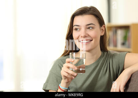 Titulaire d'un des ados distraits en verre à côté de l'eau assis sur un canapé dans la salle de séjour à la maison Banque D'Images