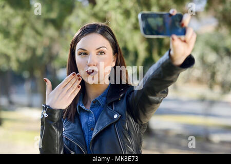 Portrait d'une belle jeune femme dans le parc avec selfies un téléphone intelligent. Girl blowing a kiss. Banque D'Images