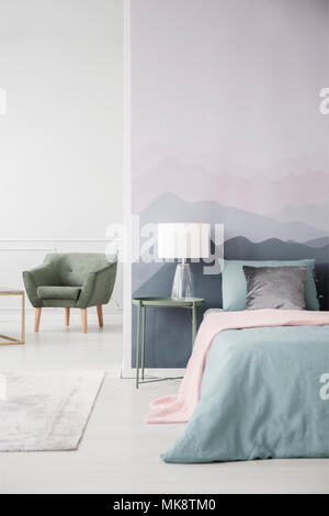 Couverture rose sur le lit à côté d'une table verte avec lampe contre mur de montagne dans la chambre avec un fauteuil d'intérieur Banque D'Images