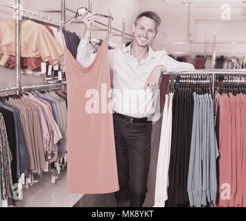 Young smiling man helping copine à choisir dans le magasin de vêtements robe Banque D'Images