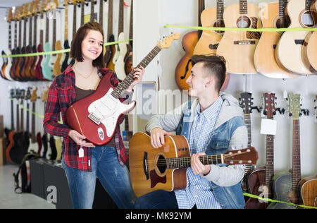Les clients d'adolescent espagnol positif comparer ampli et guitare acoustique en guitare shop Banque D'Images