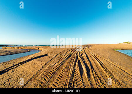 Motifs et texture des pistes de véhicules sur le sable de la plage entre l'eau de l'estuaire bleu horizon côtier contre Banque D'Images