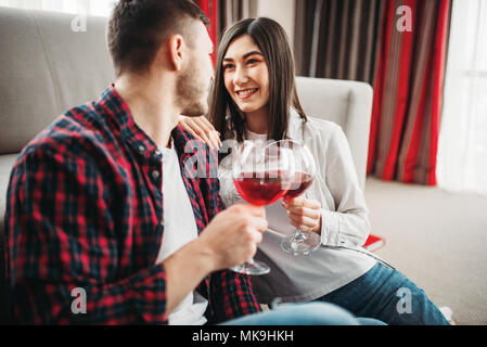 Love couple assis sur le sol contre la table, montres de film et de boissons vin rouge de grands verres, fenêtre et un salon intérieur sur l'arrière-plan. Rom Banque D'Images