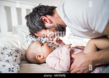 Père avec un bébé fille sur le lit chez lui à l'heure du coucher. Banque D'Images