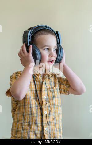 Un garçon de 4 ans dans une chemise attentivement à l'écoute de la musique au casque noir grand. Petit garçon à écouter de la musique dans big black casque. Banque D'Images