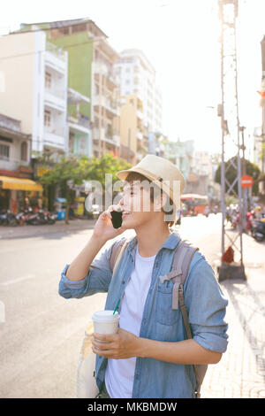 Beau jeune homme souriant à boire du café et à l'aide de smart phone Banque D'Images