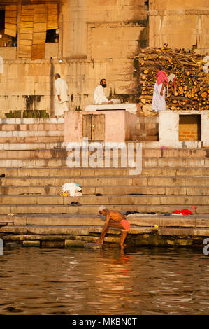 Un homme âgé se lave dans le Gange à Varanasi comme un autre homme de prières. Le tas de bois est pour les crémations qui se déroulent juste hors du châssis. Banque D'Images