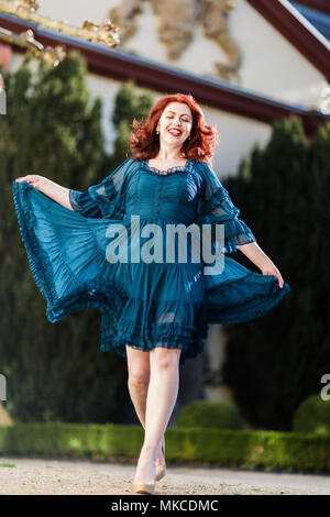 Heureux redheaded femme marche dans un parc avec dress Banque D'Images