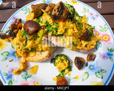 Brouillés œufs perse avec les oignons et le brocoli souches tendres servis avec des champignons frits sur du pain au levain grillé sur une plaque à motifs de fleurs Banque D'Images