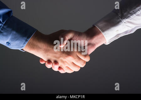 Low angle view of businessmen shaking hands sur fond gris foncé et de source de lumière à côté inférieur Banque D'Images
