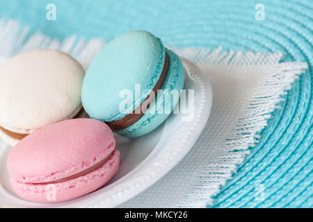 Trois macarons de différentes couleurs et goûts différents dans une assiette blanche, blanc vintage serviette. Banque D'Images