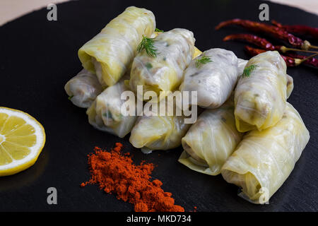 Délicieux petit chou farci feuilles (la traditionnelle dolma de la cuisine méditerranéenne) sur noir plat avec l'aneth, le poivre rouge et citron Banque D'Images