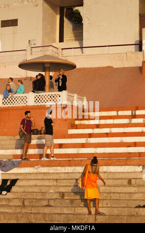 Le saint homme en bas de l'étapes semble être l'intrus parmi les touristes étrangers à Varanasi. Banque D'Images