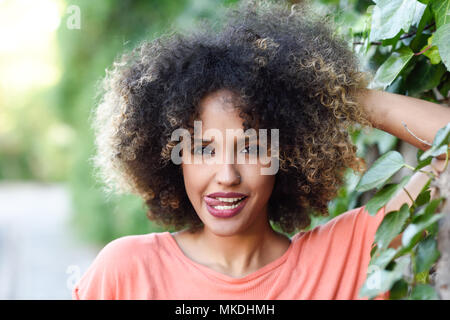 Femme noire avec la langue dans un parc urbain. Jeune fille mixte avec afro coiffure. Drôle de sexe féminin. Banque D'Images