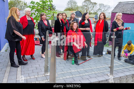 L'ensemble chœur de femmes d'effectuer à l'extérieur dans un festival de musique annuel de jazz à Ballydehob, Irlande. Les femmes sont habillées en costume rouge et noir. Banque D'Images