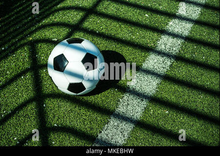 Ballon de football classique noir et blanc avec des ombres sur le terrain d'un but de football artificiel Banque D'Images