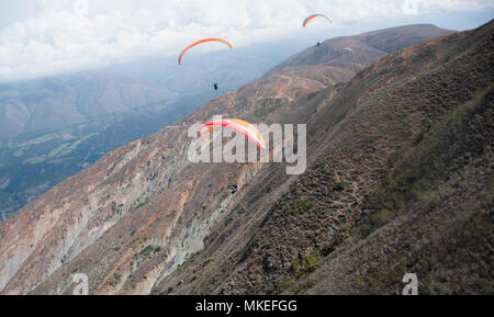 Trois immenses parapentes sont orange volant le long de la pente d'une montagne sur la vallée. Banque D'Images