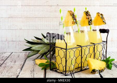 Jus d'ananas dans la bouteille de lait avec une paille dans un panier métallique contre un arrière-plan en bois blanc Banque D'Images