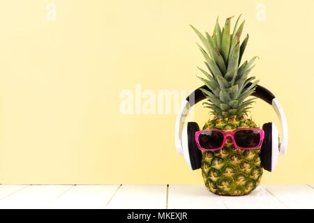 L'ananas avec des lunettes de Hipster et casque sur fond jaune. Concept d'été minime. Banque D'Images