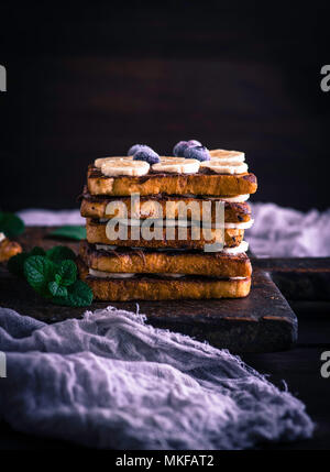 Poêlée de morceaux de pain blanc dans un œuf avec le lait et enduit de chocolat, pain doré avec une banane sur une planche en bois brun Banque D'Images