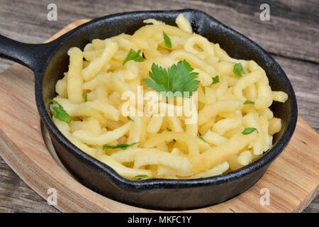 Spaetzle avec du beurre et le persil dans une poêle de fer de planche à découper en bambou close up Banque D'Images