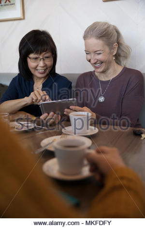 Souriant, senior women friends using digital tablet at cafe
