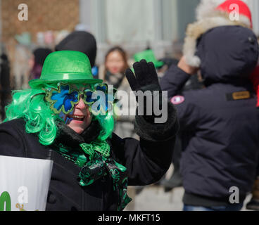 Un smiling woman wearing green hat et shmrock lunettes en forme de forme à la foule dans la parade de la St Patrick à Montréal Banque D'Images