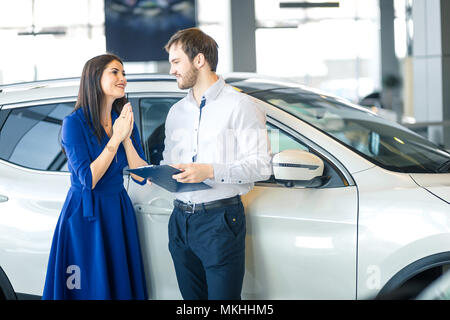 Jeune femme au foyer heureux de remercier son mari pour son joli présent- une nouvelle voiture en car showroom Banque D'Images
