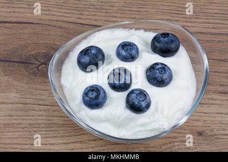 Myrtilles sucré dans du yogourt nature. Yaourt blanc dans le bol en verre avec les bleuets délicieux sur un fond de bois vintage. Banque D'Images