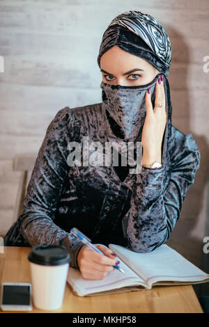 Jeune femme musulmane écrit sur son ordinateur portable en cafe Banque D'Images