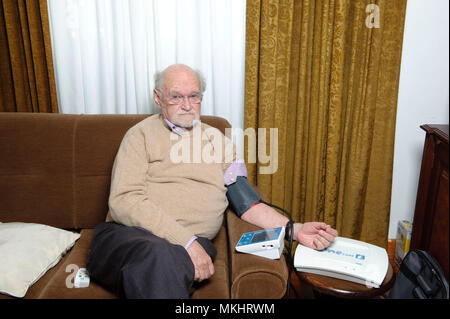 L'homme contrôle de sa pression artérielle à domicile avec un sphygmomanomètre électronique Banque D'Images