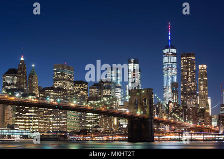 Le Pont de Brooklyn et de Manhattan Skyline illuminée le soir avec ciel bleu et lisse la surface de l'eau coup de côté de Brooklyn, New York, USA. Banque D'Images