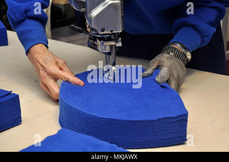 Une couturière utilise un couteau vertical pour découper un tas de tissus pour vestes dans une salle de couture. Banque D'Images