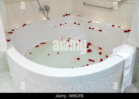 Close-up d'une grande baignoire jacuzzi blanc décoré avec des pétales de rose rouge Banque D'Images