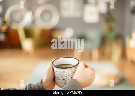 Close-up de personne tenant une tasse du métal avec plateau sur l'arrière-plan de salon floue Banque D'Images