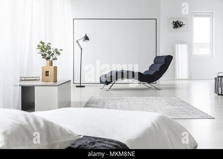 À côté de black chaise longue dans l'intérieur d'espace ouvert avec un lit blanc et des plantes sur une table Banque D'Images