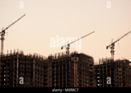 3 Bâtiments en construction avec le béton et le fer de skeleton et de grues de construction en haut tourné contre le ciel orange de crépuscule. Un site commun à Delhi, Delhi, Jaipur, Delhi, Chennai, Bangalore, Hyderabad, Gujarat Banque D'Images