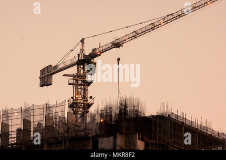 Grue sur le haut d'un bâtiment en construction tourné contre le ciel orange de crépuscule. Le cadre de l'immeuble est exposé et de la grue est bien visible Banque D'Images