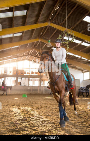 Jeune femme rides son cheval dans le manège. Dans l'arrière-plan vous pouvez voir plusieurs brouillé les chevaux et les cavaliers. Le rider trotskistes sur son Hanovre. Sh Banque D'Images