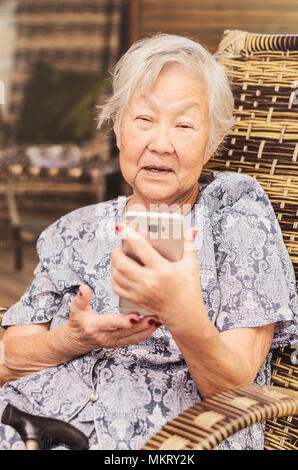 Vieille dame assis à la maison l'apprentissage de l'utilisation du smartphone. Obaasan (grand-mère), le japonais descendant. Banque D'Images
