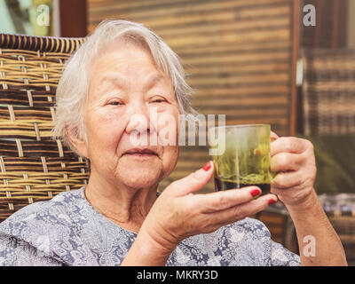 Vieille dame assis confortablement à la maison tenant une tasse de café noir. Banque D'Images