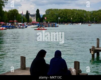 Deux femmes musulmanes en vacances, peut-être à partir de la région du Golfe. Chaque port d'un hijab, abaya et assis sur un quai le long du lac d'Annecy, France Banque D'Images