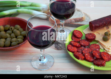 Deux verres de vin rouge avec des saucisses, du fromage et du pain et d'olives vertes sur une table Banque D'Images