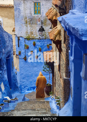 L'homme à un imperméable, une photographie de son dos, descend l'escalier en pierre bleue entre les murs de la médina de Chefchaouen, Maroc. Banque D'Images