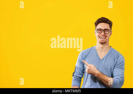 Jeune homme hipster dans les verres et le cavalier bleu pointant loin heureusement sur fond jaune orange Banque D'Images