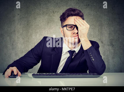 Young man sitting at table in office à la recherche désespéré et épuisé. Banque D'Images