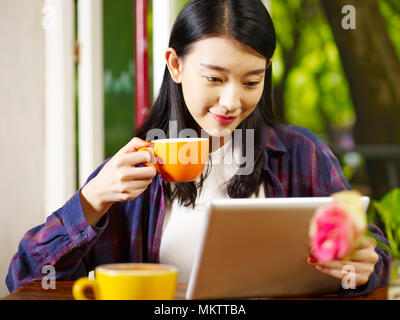 Beautiful young asian woman using digital tablet en buvant un cappuccino au café. Banque D'Images