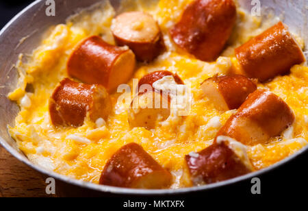 Petit-déjeuner d'œufs brouillés et saucisses dans une casserole sur fond noir. Banque D'Images