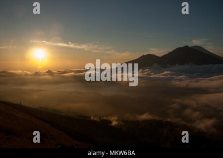 Comme le soleil se lève au-dessus de l'horizon, la lumière se propage à travers les nuages bas sur le lac Batur. À proximité, le Mont Agung commence à révéler plus de texture. Banque D'Images